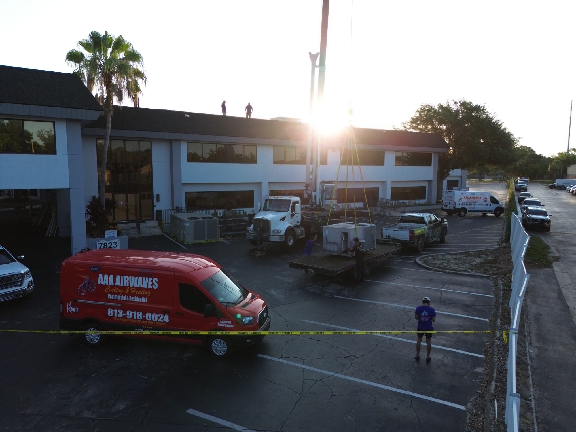 AAA Airwaves crew and crane lifting a rooftop HVAC unit at a two-story office building